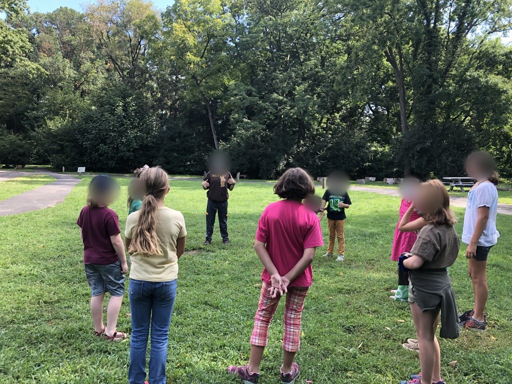 Children, faces blurred, standing in a circle in a park