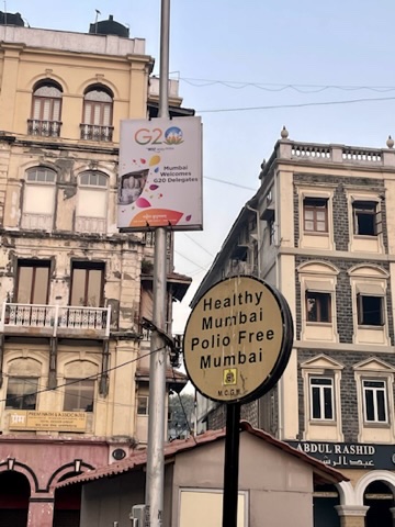 Street sign reading Healthy Mumbai, Polio Free Mumbai, beside a G20 welcome banner