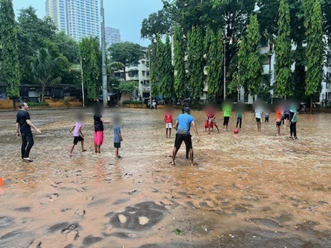 Children, faces blurred, playing soccer on a flooded field in the rain